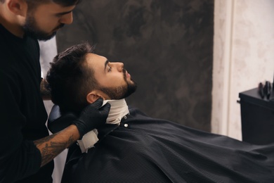 Photo of Professional hairdresser using cold towel to calm client's skin after shaving in barbershop