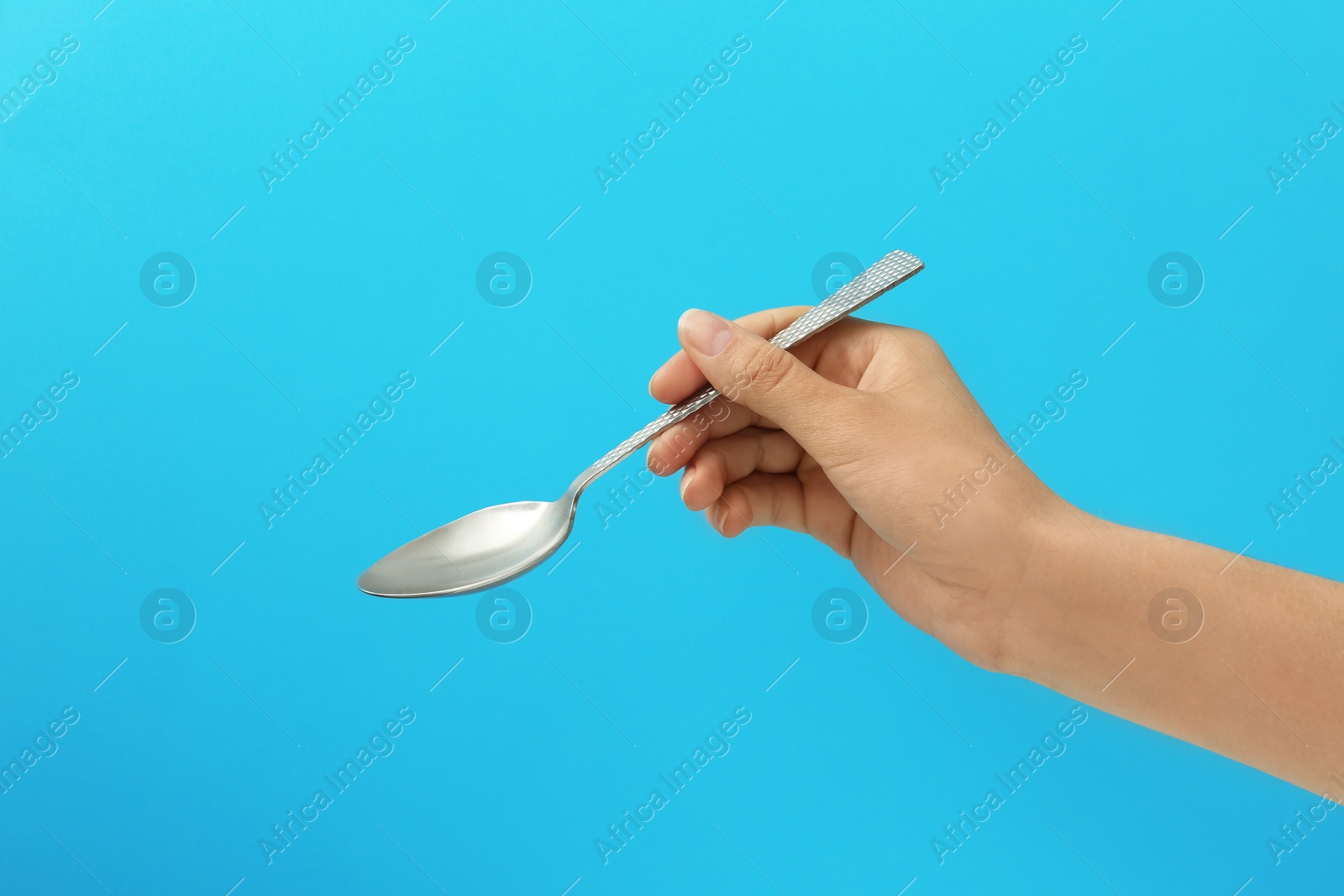 Photo of Woman holding empty table spoon on color background, closeup