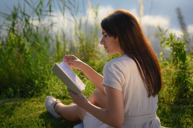 Young woman reading book near lake on sunny day