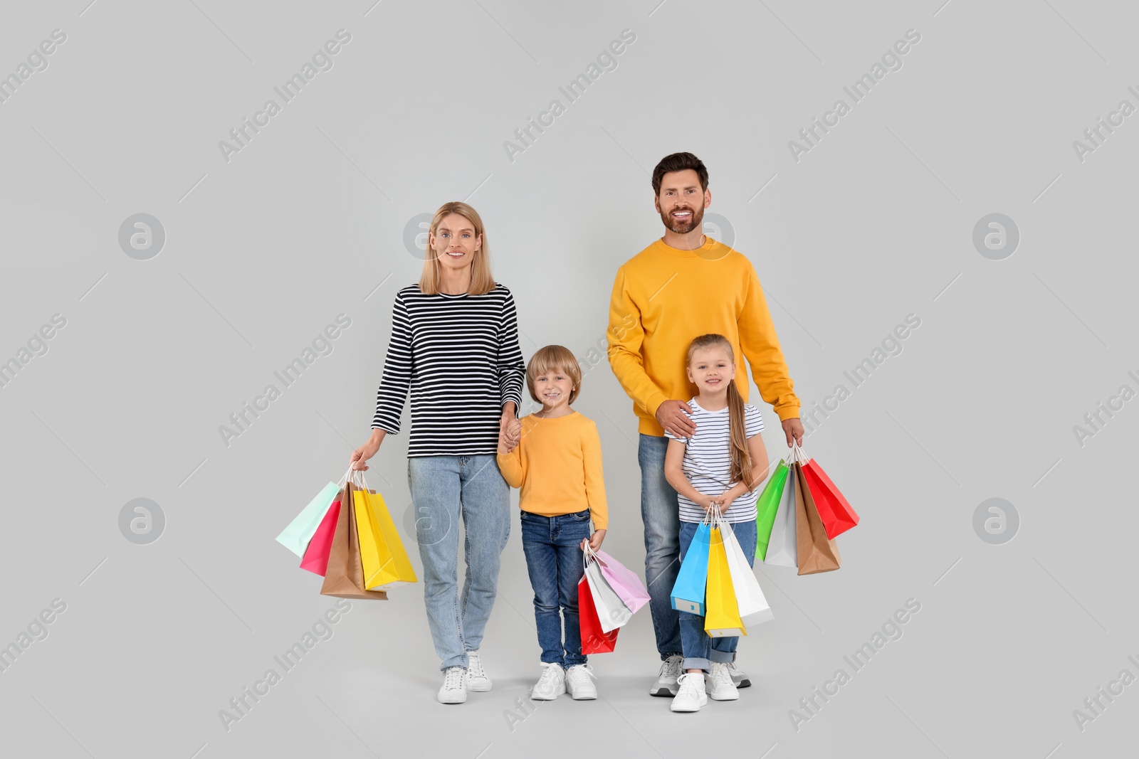 Photo of Family shopping. Happy parents and children with many colorful bags on light grey background