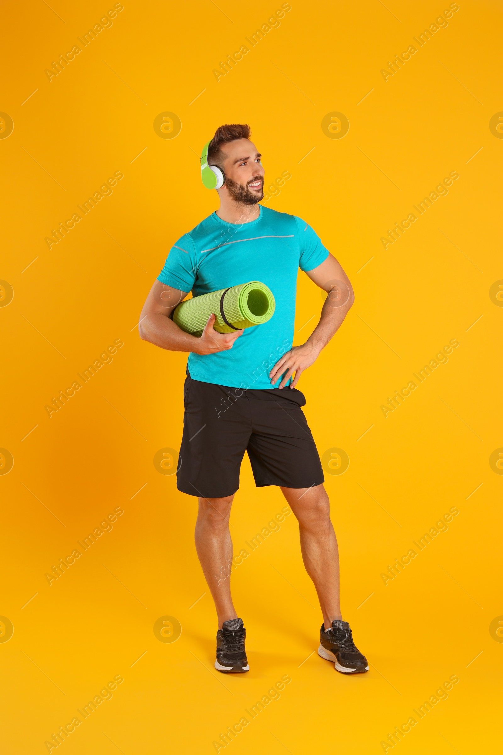 Photo of Handsome man with yoga mat and headphones on yellow background
