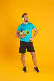 Handsome man with yoga mat and headphones on yellow background