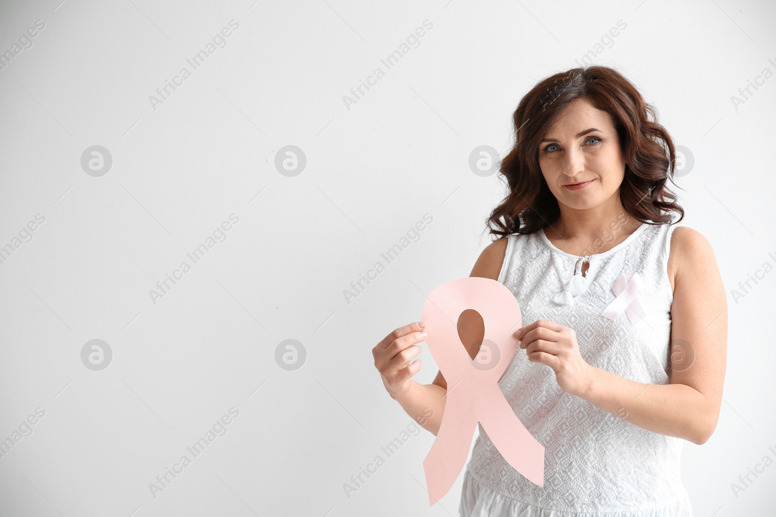 Photo of Woman with pink paper ribbon and space for text on white background. Breast cancer awareness concept