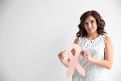 Woman with pink paper ribbon and space for text on white background. Breast cancer awareness concept