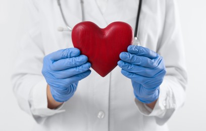 Photo of Doctor holding red heart on white background, closeup. Cardiology concept