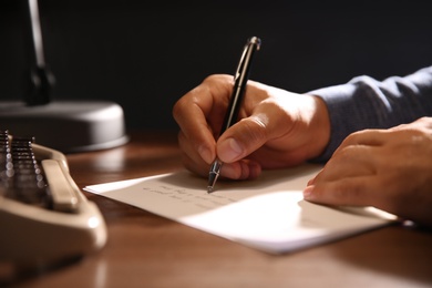 Photo of Man writing letter at wooden table indoors, closeup