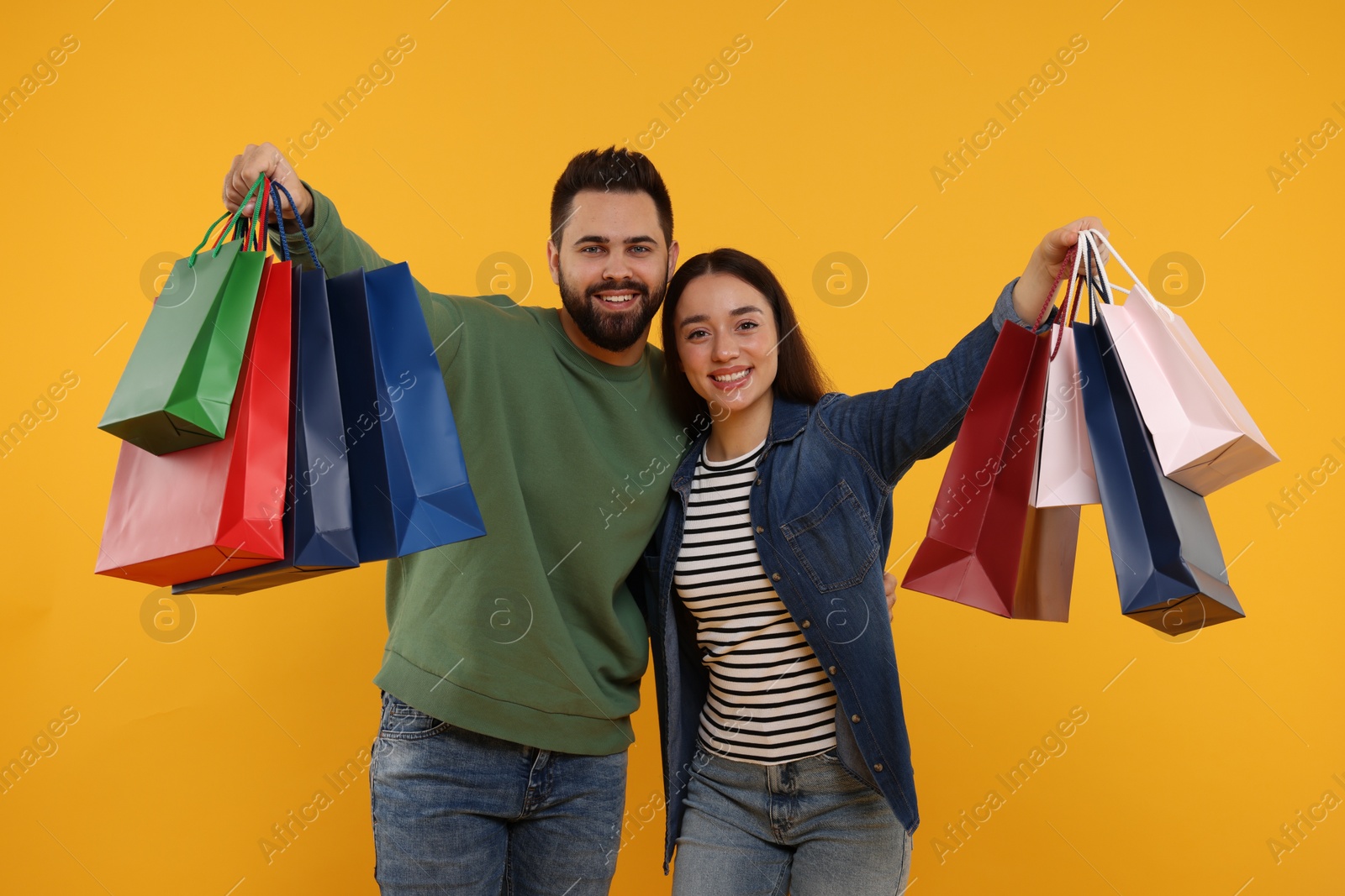 Photo of Happy couple with shopping bags on orange background