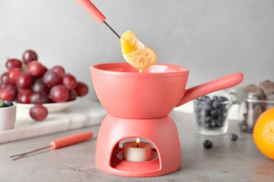 Photo of Dipping tangerine segment into pot with white chocolate fondue on table