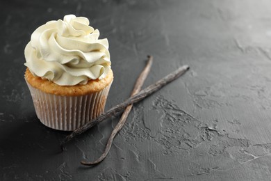 Photo of Tasty cupcake with cream and vanilla pods on black table, closeup. Space for text