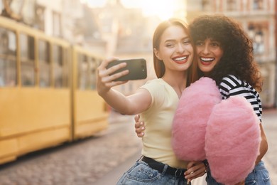 Happy friends with pink cotton candies taking selfie in city on sunny day. Space for text