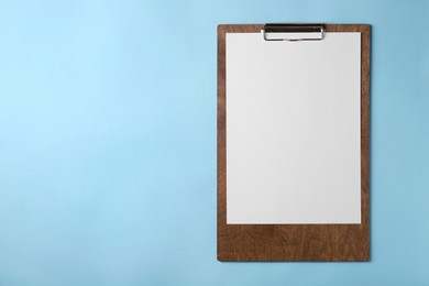 Photo of New wooden clipboard with sheet of blank paper on light blue background, top view. Space for text