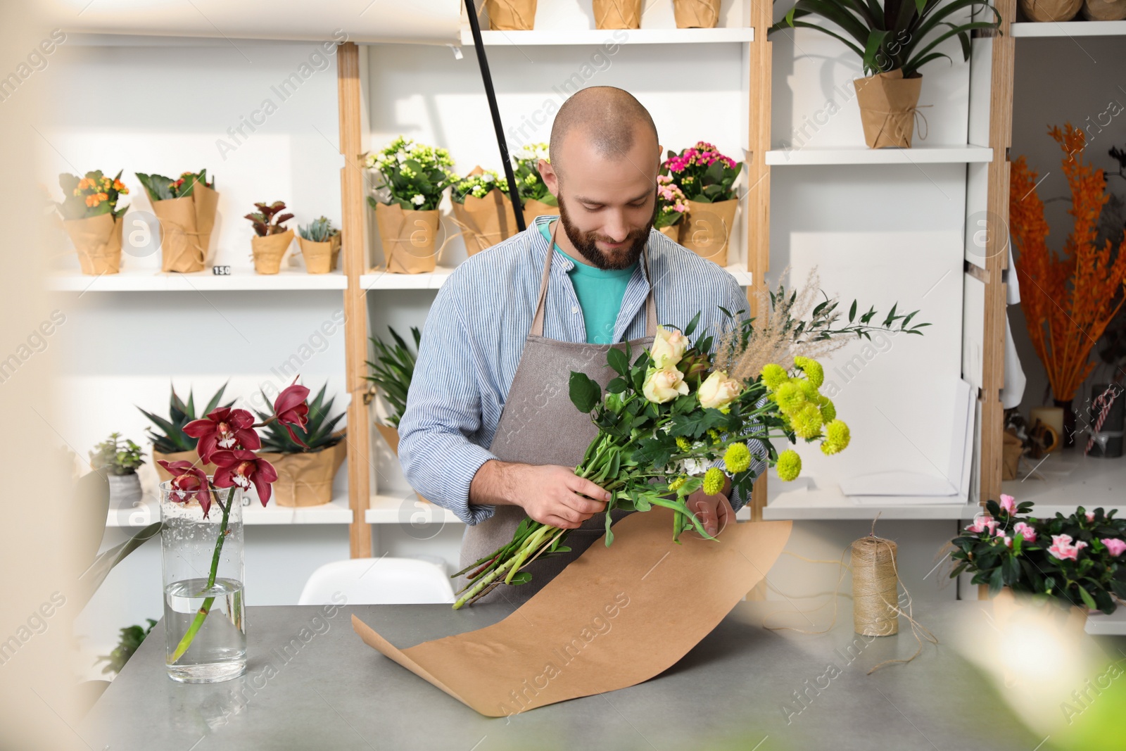 Photo of Florist making bouquet with fresh flowers at table in shop