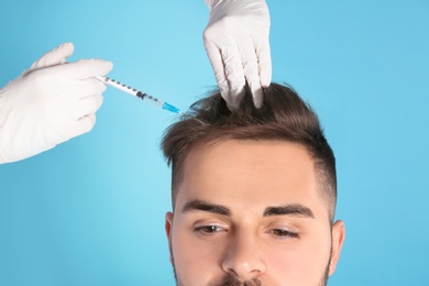 Photo of Young man with hair loss problem receiving injection on color background, closeup