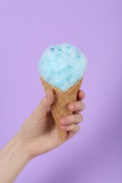 Woman holding waffle cone with cotton candy on violet background, closeup