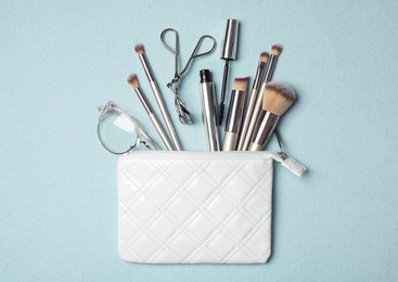 Photo of Cosmetic bag with makeup products and beauty accessories on light blue background, flat lay