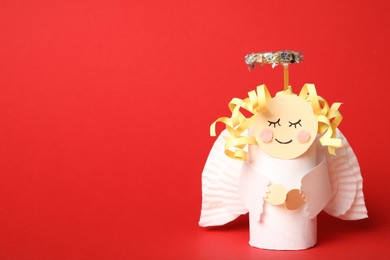 Photo of Toy angel made of toilet paper hub on red background. Space for text