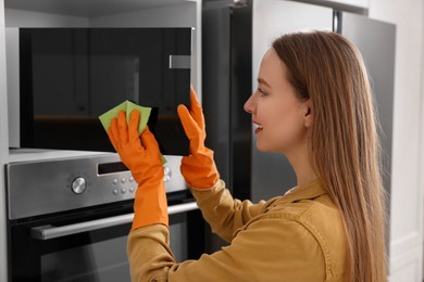 Photo of Woman with microfiber cloth cleaning microwave in kitchen