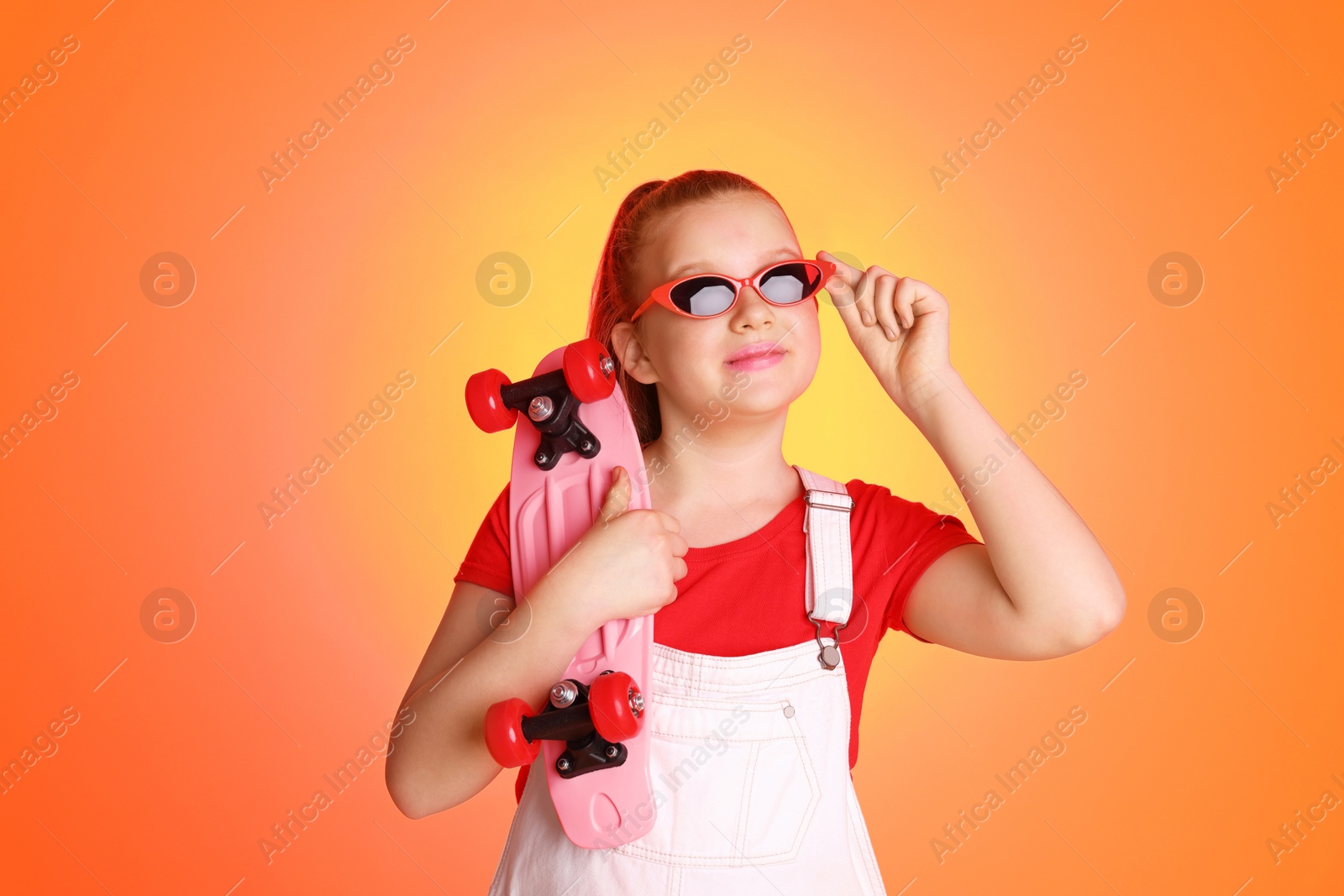 Photo of Cute indie girl with sunglasses and penny board on color background