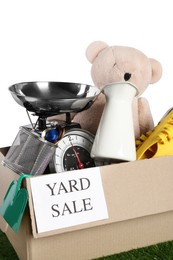 Photo of Sign Yard Sale written on box with different stuff on green grass against white background, closeup