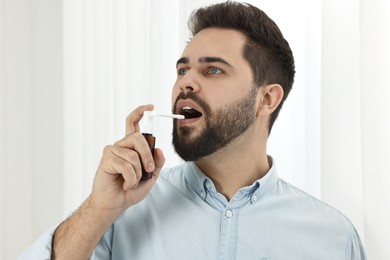 Young man using throat spray at home