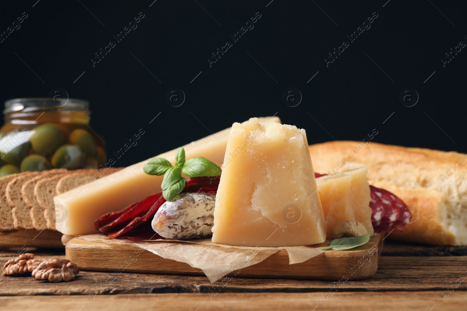 Photo of Delicious parmesan cheese, sausage, olives and basil on wooden table