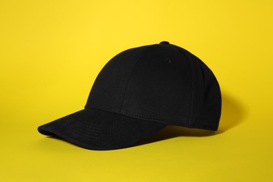 Photo of Stylish black baseball cap on yellow background