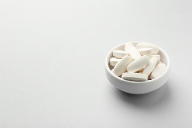 Photo of Vitamin pills in bowl on grey background. Space for text