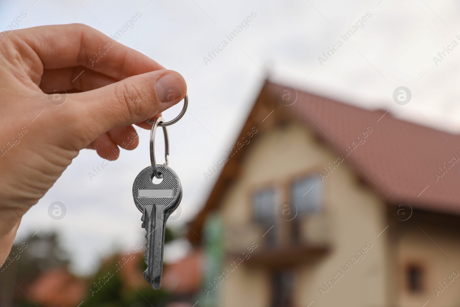 Photo of Real estate agent holding keys to new house outdoors, closeup. Space for text