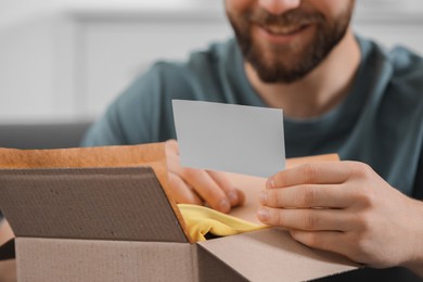 Photo of Man holding greeting card near parcel with Christmas gift, closeup