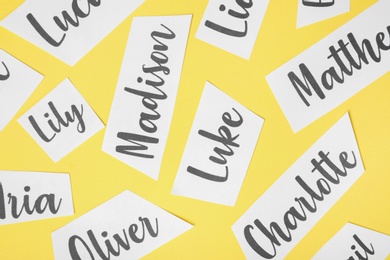 Paper sheets with written different baby names on yellow background, flat lay