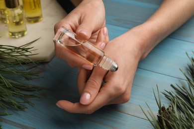 Photo of Woman applying pine essential oil on hand at light blue wooden table, closeup