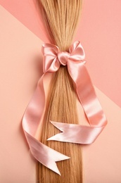 Photo of Blond hair tied with ribbon on color background, top view