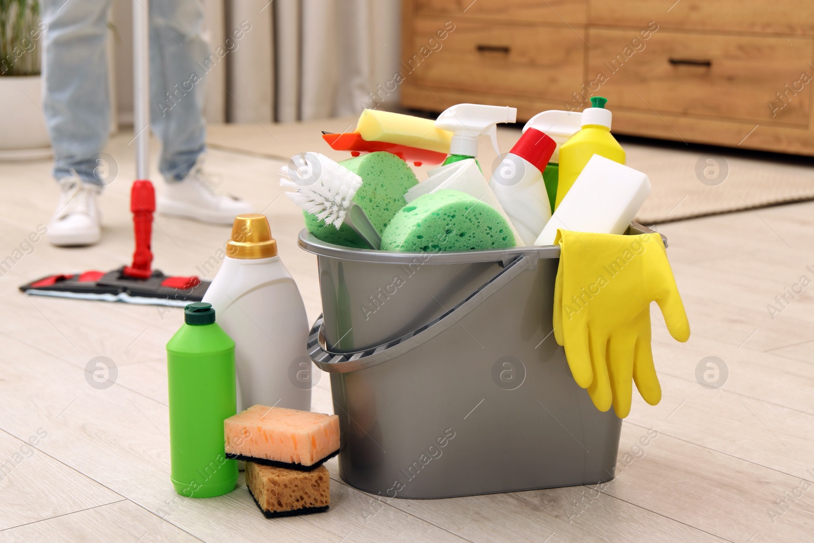 Photo of Different cleaning supplies in bucket and woman mopping floor, selective focus