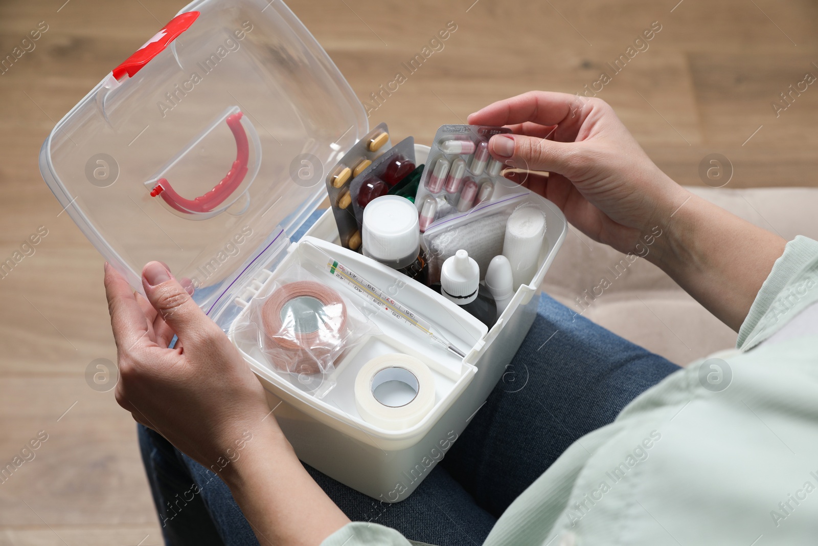 Photo of Woman putting pills into first aid kit indoors, closeup