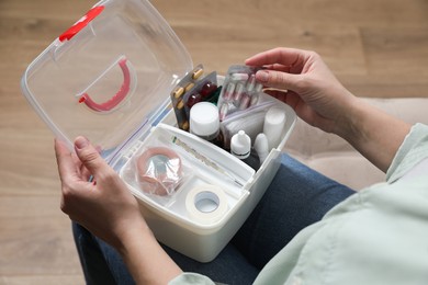 Photo of Woman putting pills into first aid kit indoors, closeup