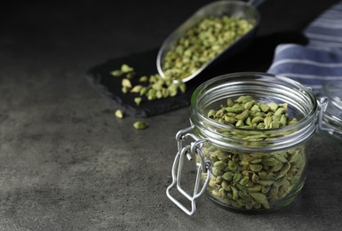 Glass jar with dry cardamom pods on dark grey table, space for text