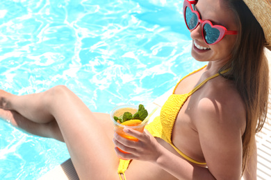 Photo of Woman with glass of refreshing drink near swimming pool, closeup