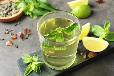 Photo of Glass with hot aromatic mint tea, fresh leaves and lime on table