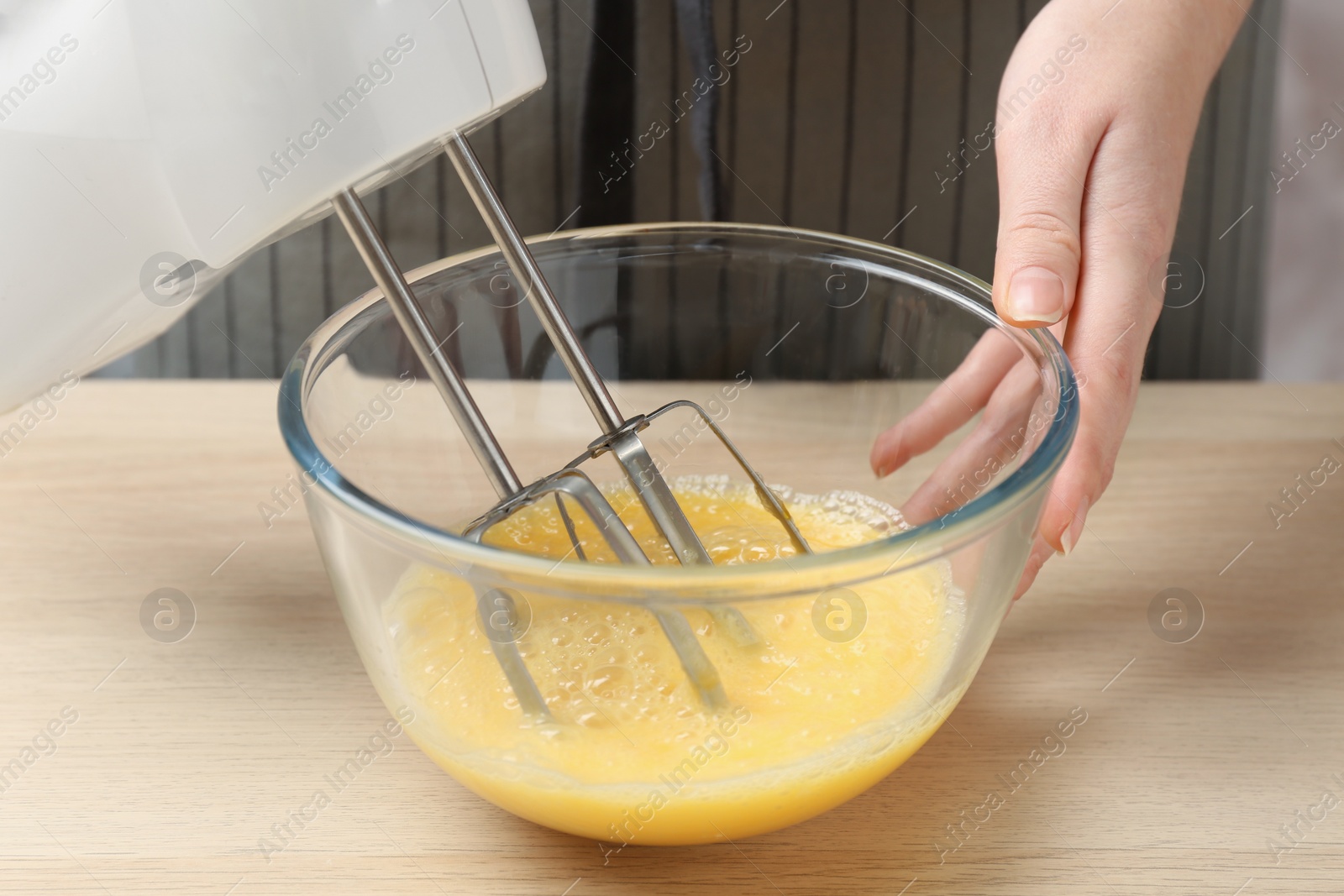 Photo of Woman beating eggs with mixer at wooden table, closeup