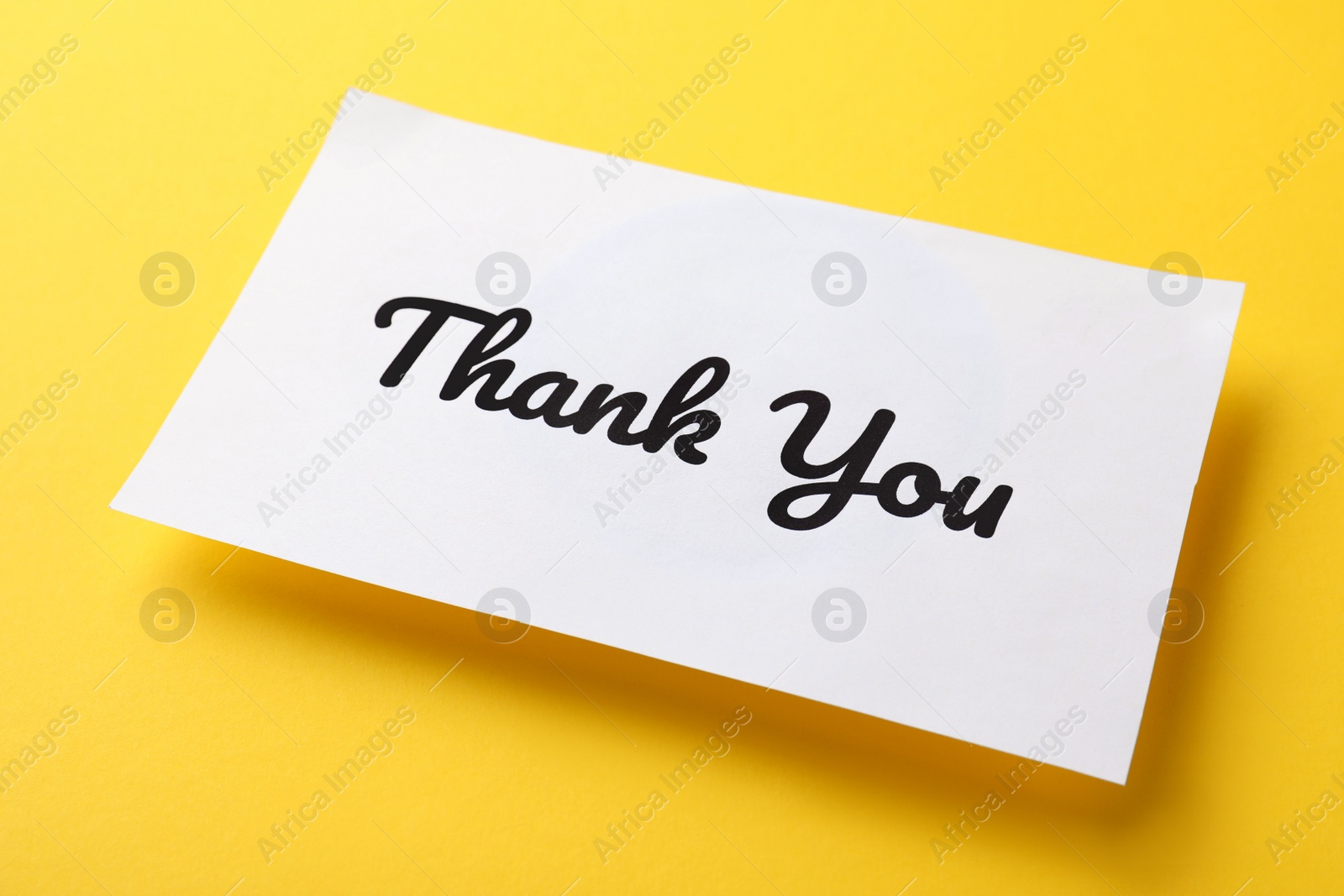 Photo of White paper note with phrase Thank You on yellow background