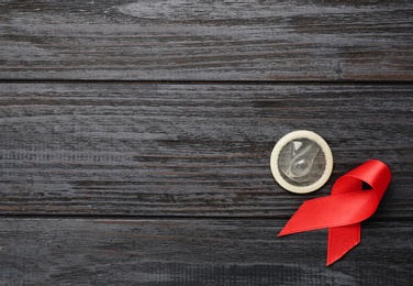 Photo of Red ribbon and condom on black wooden background, flat lay with space for text. AIDS disease awareness
