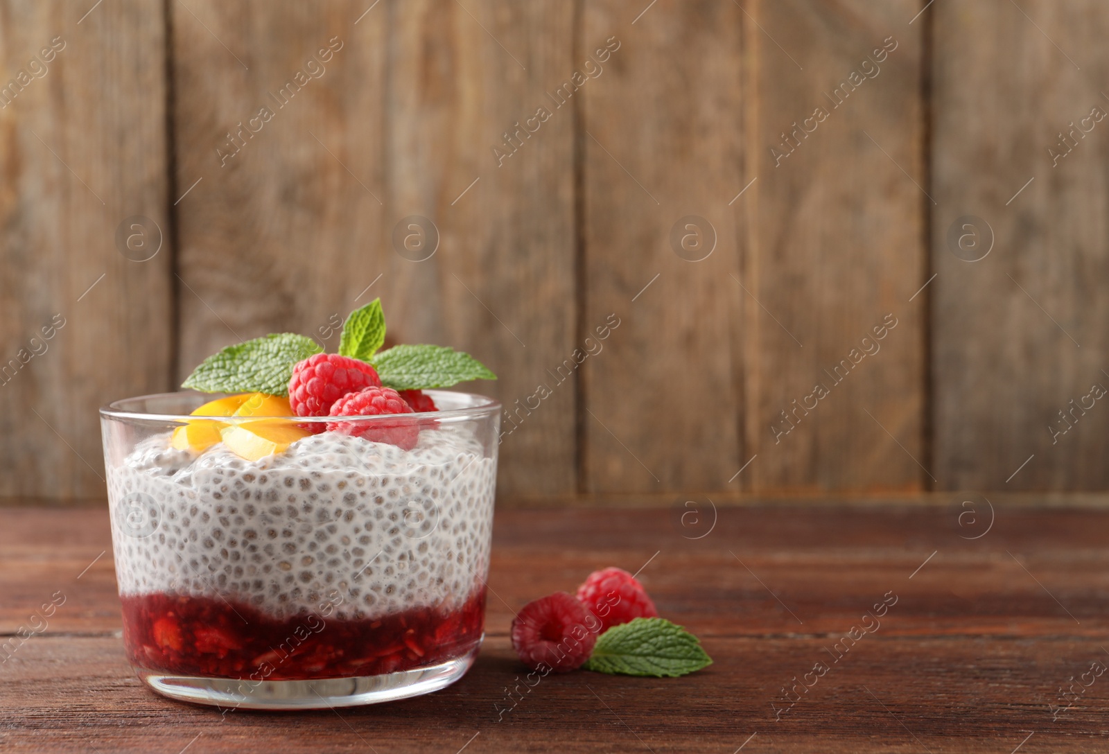 Photo of Delicious chia pudding with raspberries, peach and mint on wooden table, space for text