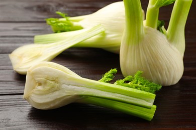 Whole and cut fennel bulbs on wooden table, closeup