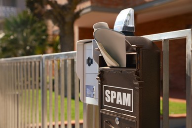 Image of Mailbox with word Spam and newspaper on fence near house