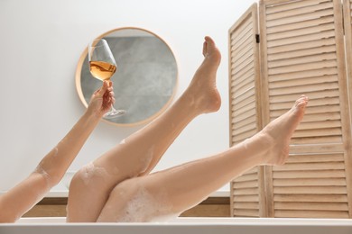 Woman with glass of wine taking bath in tub indoors, closeup