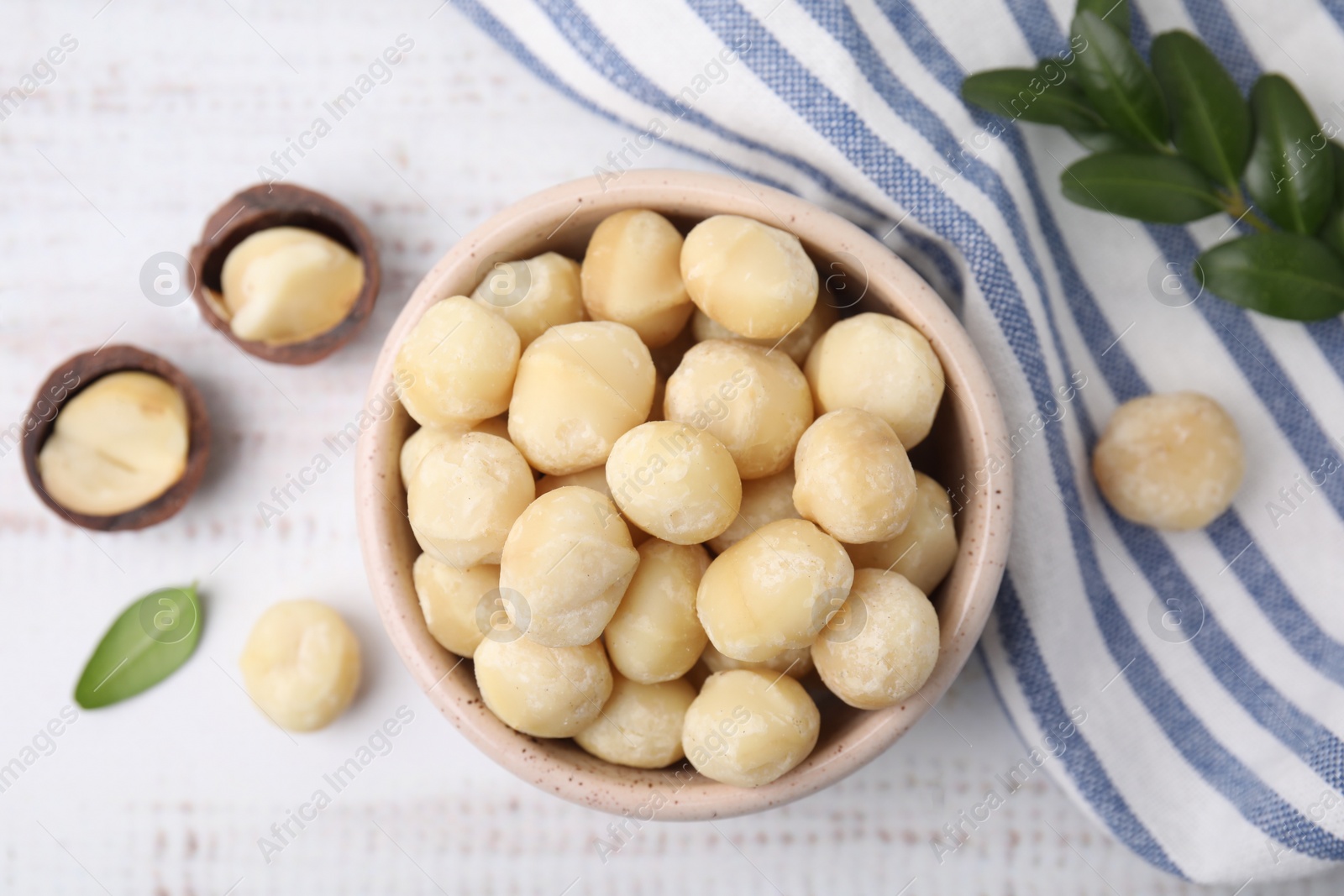 Photo of Tasty peeled Macadamia nuts in bowl on light table, flat lay