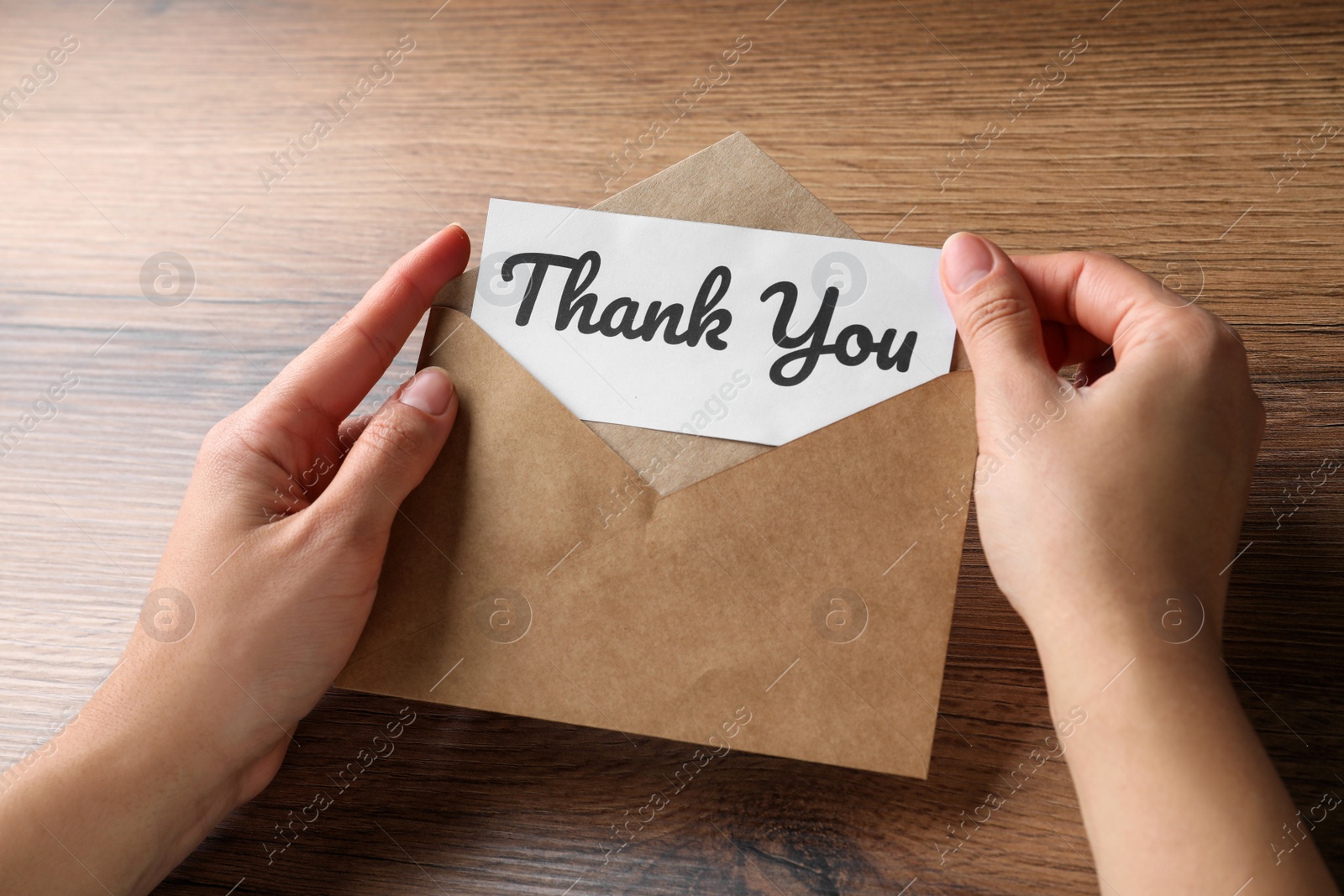 Photo of Woman holding envelope and card with phrase Thank you at wooden table, closeup