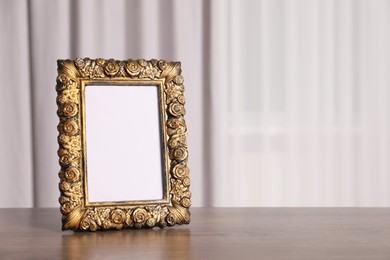 Photo of Beautiful vintage empty frame on wooden table indoors, space for text