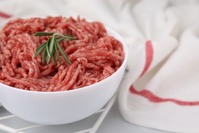 Fresh raw ground meat and rosemary in bowl on light table, closeup. Space for text