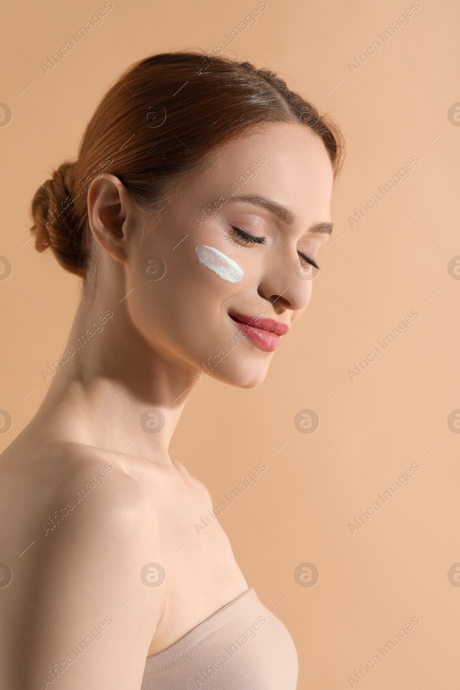 Photo of Beautiful young woman with sun protection cream on her face against beige background